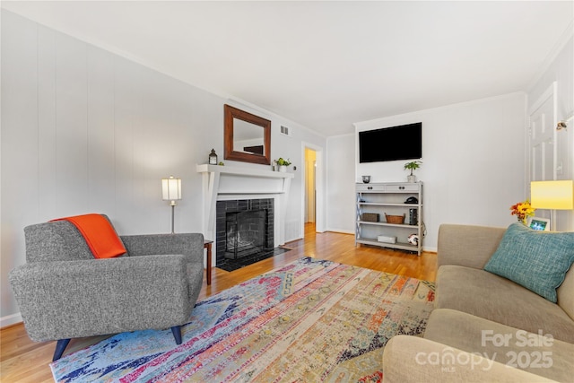 living area with a fireplace with flush hearth, visible vents, crown molding, and wood finished floors