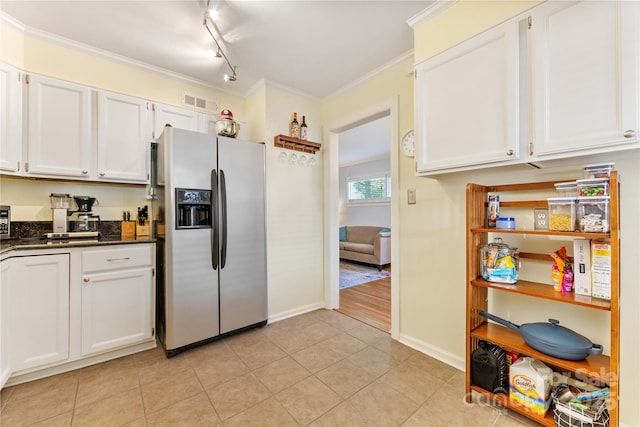 kitchen with stainless steel fridge, dark countertops, crown molding, white cabinetry, and light tile patterned flooring