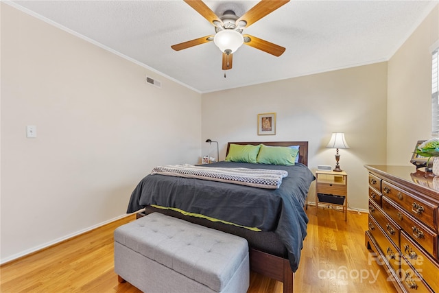 bedroom featuring light wood finished floors, baseboards, visible vents, and ornamental molding