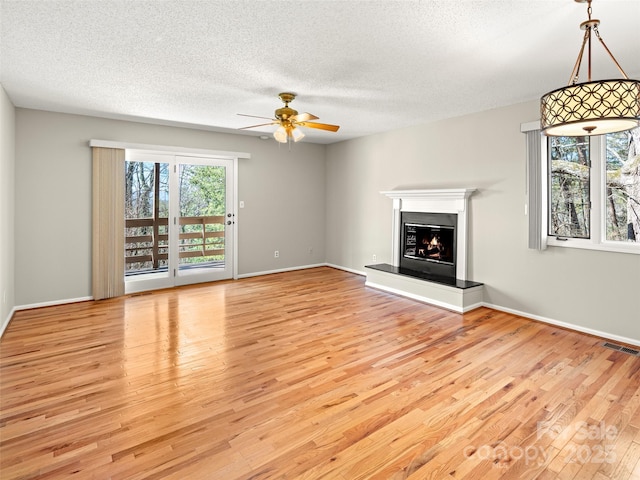 unfurnished living room with visible vents, a glass covered fireplace, ceiling fan, wood finished floors, and a textured ceiling