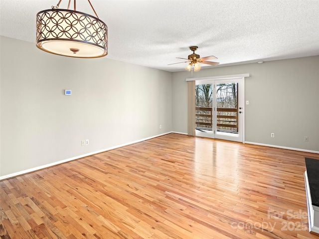 unfurnished room with ceiling fan, a textured ceiling, baseboards, and wood finished floors