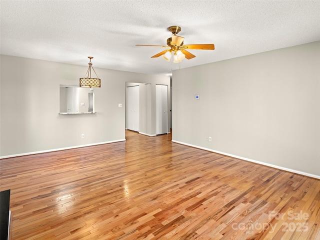 empty room featuring light wood-type flooring, ceiling fan, baseboards, and a textured ceiling