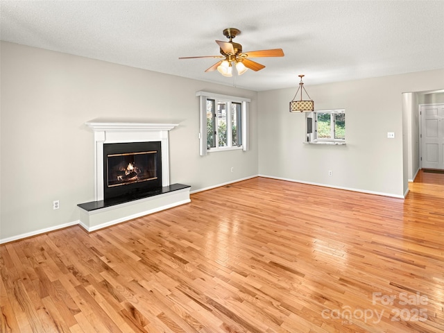 unfurnished living room with light wood finished floors, a wealth of natural light, and a glass covered fireplace