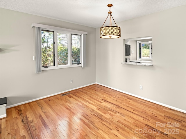 empty room with a healthy amount of sunlight, wood-type flooring, visible vents, and baseboards