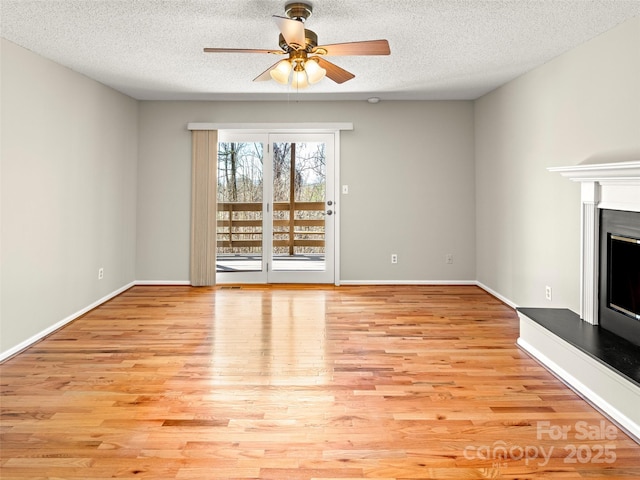 unfurnished living room featuring a textured ceiling, baseboards, a fireplace with raised hearth, and wood finished floors