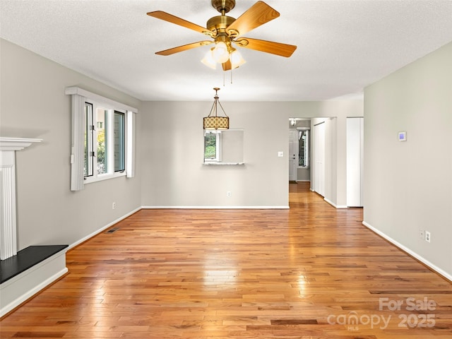 unfurnished living room with a textured ceiling, baseboards, a ceiling fan, and light wood-style floors