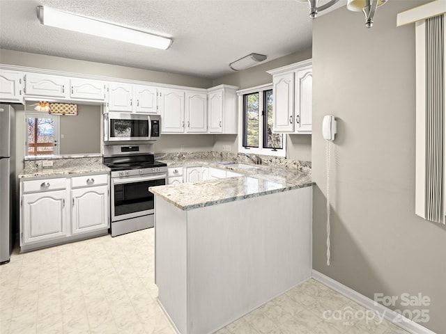 kitchen with a peninsula, appliances with stainless steel finishes, light floors, and white cabinetry