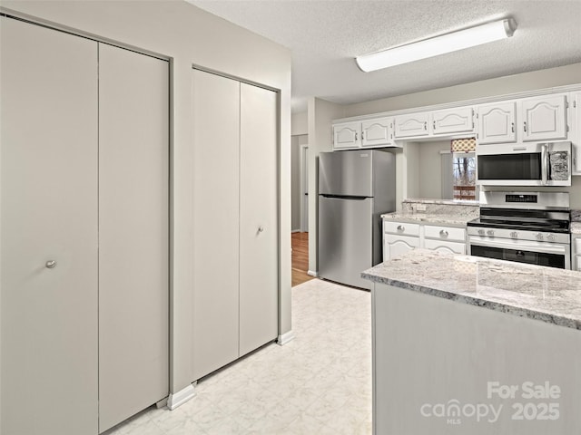 kitchen featuring light floors, appliances with stainless steel finishes, white cabinets, a textured ceiling, and light stone countertops