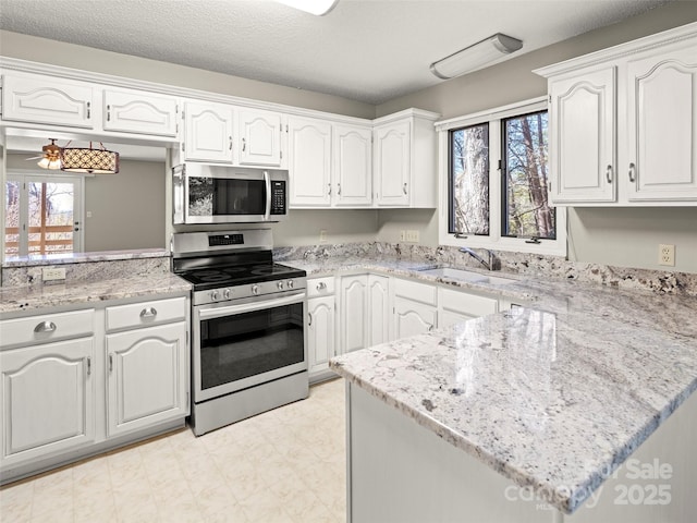 kitchen with appliances with stainless steel finishes, a peninsula, light floors, white cabinetry, and a sink