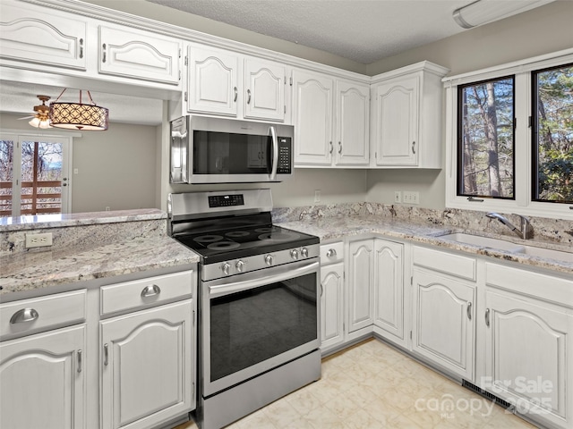 kitchen featuring white cabinets, a ceiling fan, appliances with stainless steel finishes, light stone counters, and a sink