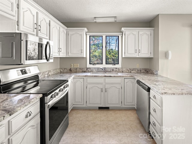 kitchen featuring light stone counters, stainless steel appliances, white cabinets, a sink, and a peninsula