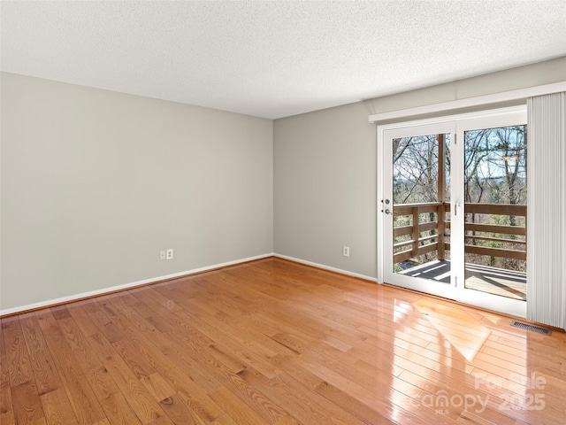 empty room featuring baseboards, visible vents, light wood-style flooring, and a textured ceiling