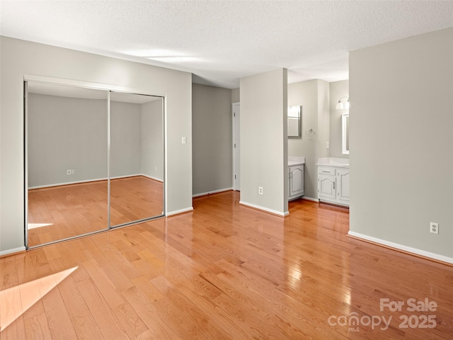 unfurnished bedroom featuring a closet, light wood-style flooring, ensuite bathroom, a textured ceiling, and baseboards