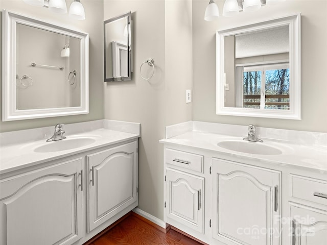 bathroom featuring wood finished floors, two vanities, a sink, and baseboards