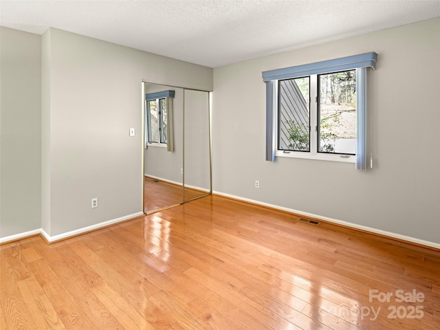 unfurnished bedroom with baseboards, visible vents, a textured ceiling, light wood-type flooring, and a closet