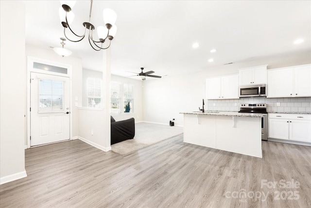 kitchen with tasteful backsplash, appliances with stainless steel finishes, light wood-style flooring, and light stone counters