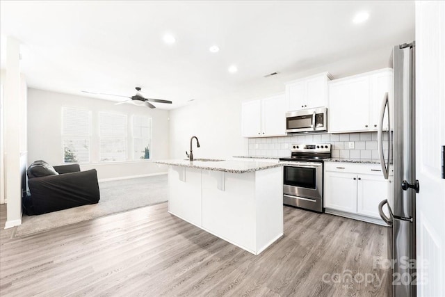 kitchen featuring tasteful backsplash, light stone counters, open floor plan, stainless steel appliances, and a sink