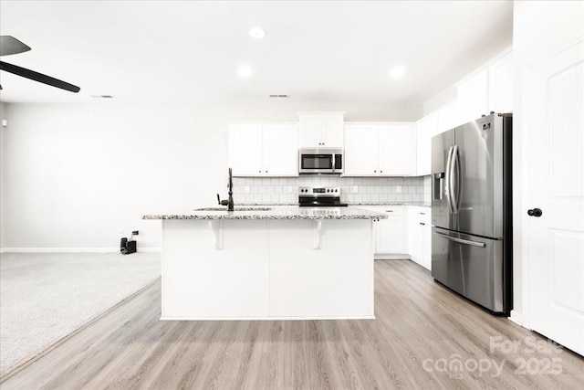 kitchen with light stone counters, stainless steel appliances, a sink, decorative backsplash, and a kitchen bar