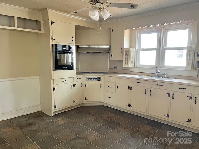 kitchen featuring light countertops, crown molding, under cabinet range hood, a sink, and black oven