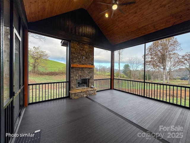 unfurnished sunroom with vaulted ceiling, ceiling fan, an outdoor stone fireplace, and wood ceiling