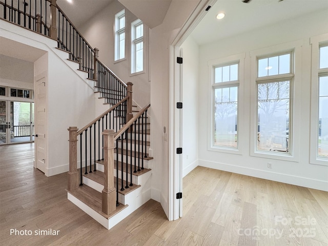 stairway with a towering ceiling, baseboards, and wood finished floors