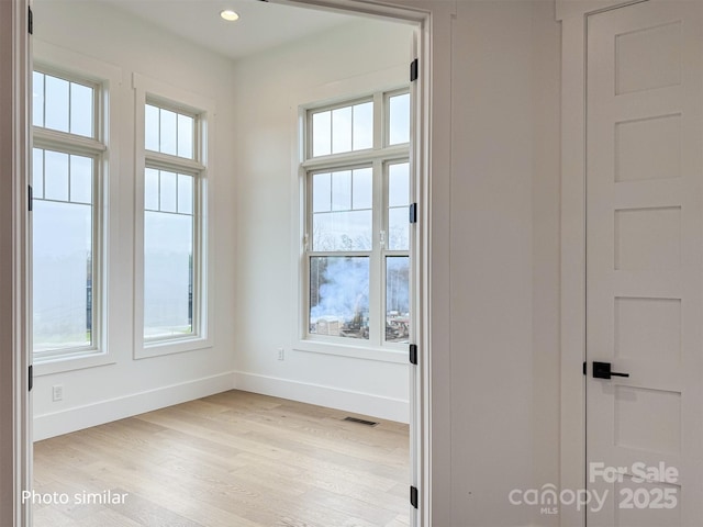 spare room with light wood-style floors, a wealth of natural light, visible vents, and baseboards