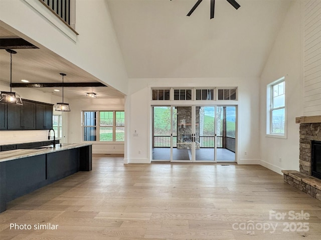 kitchen with plenty of natural light, light wood-style flooring, high vaulted ceiling, and a stone fireplace