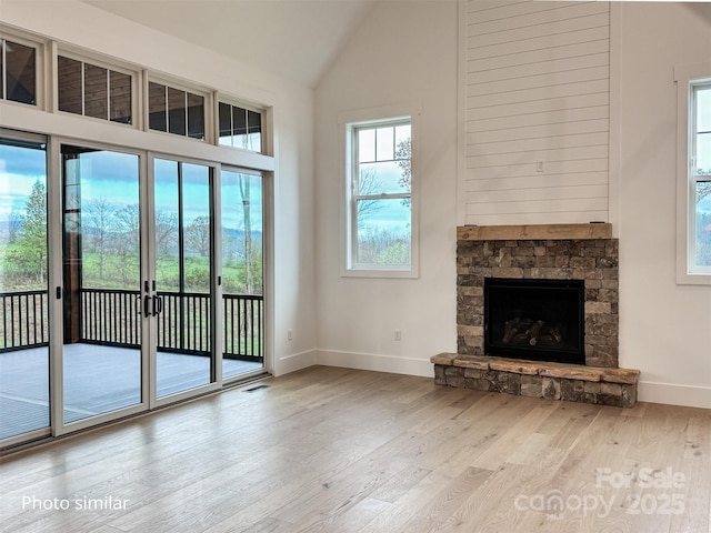 unfurnished living room with high vaulted ceiling, a stone fireplace, wood finished floors, visible vents, and baseboards