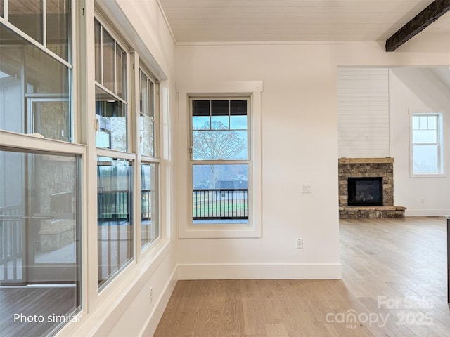 interior space with beam ceiling, a fireplace, baseboards, and wood finished floors