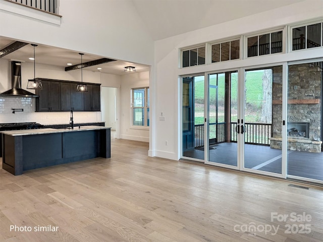 kitchen featuring light wood finished floors, tasteful backsplash, wall chimney exhaust hood, light countertops, and a sink