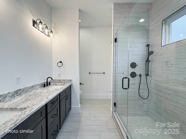 full bath with toilet, a sink, baseboards, double vanity, and a stall shower