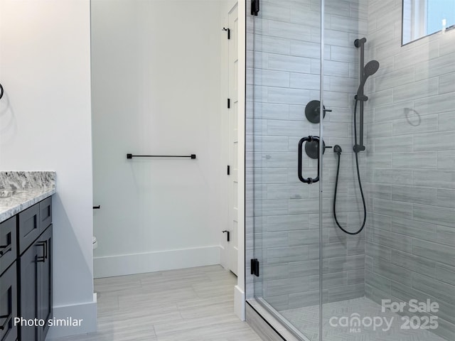 bathroom with baseboards, toilet, a shower stall, and vanity