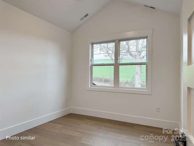 unfurnished room featuring lofted ceiling, light wood-style floors, baseboards, and visible vents