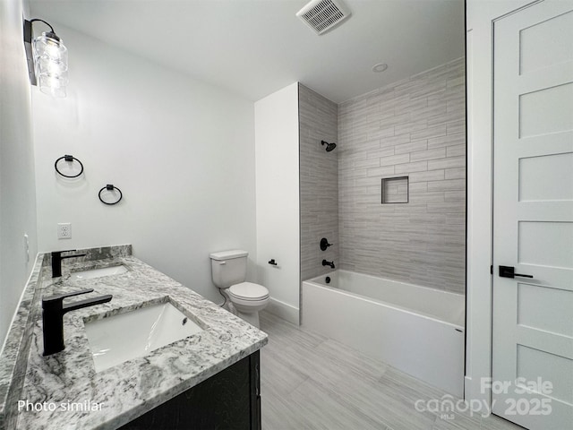 full bathroom with toilet, double vanity, visible vents, and a sink