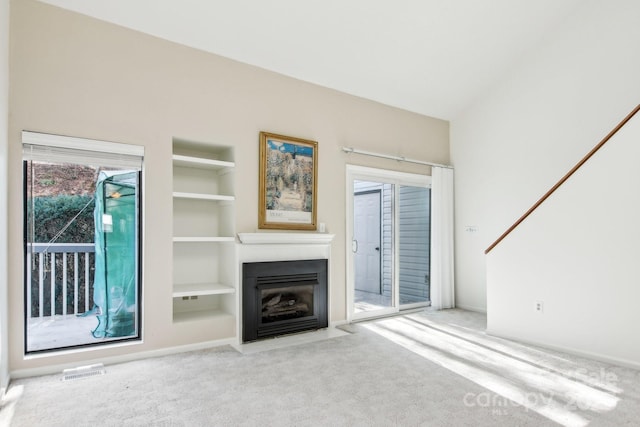 unfurnished living room with built in shelves, visible vents, a fireplace with flush hearth, and carpet floors