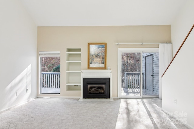 unfurnished living room with carpet flooring, built in features, baseboards, and a fireplace with flush hearth