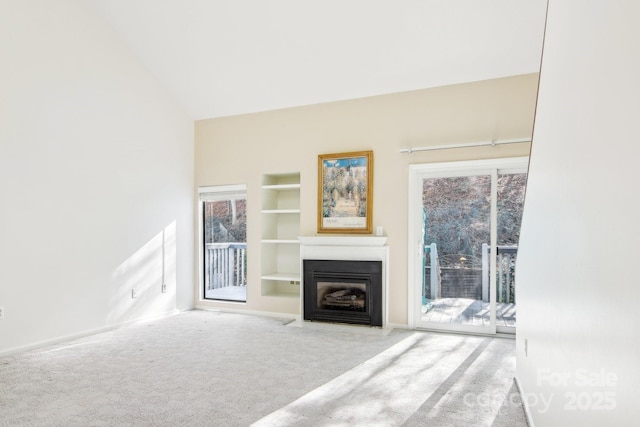 unfurnished living room with carpet flooring, built in shelves, a fireplace with flush hearth, and high vaulted ceiling