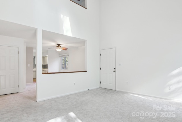 interior space featuring light carpet, baseboards, a high ceiling, and ceiling fan