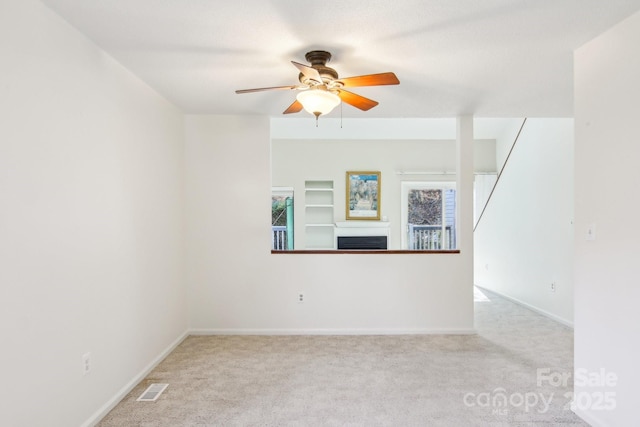 carpeted empty room with baseboards, a fireplace, visible vents, and ceiling fan