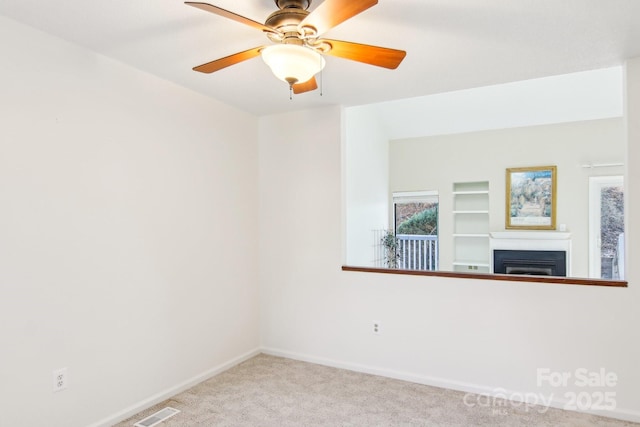 carpeted spare room featuring visible vents, a fireplace, a ceiling fan, and baseboards