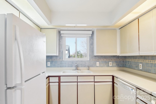 kitchen with a sink, white appliances, tasteful backsplash, and light countertops