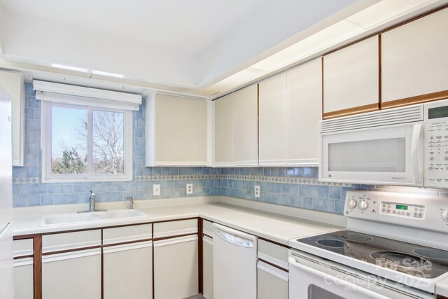 kitchen featuring backsplash, white appliances, light countertops, and a sink