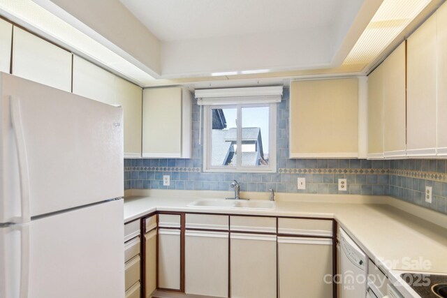 kitchen featuring a sink, decorative backsplash, light countertops, and freestanding refrigerator