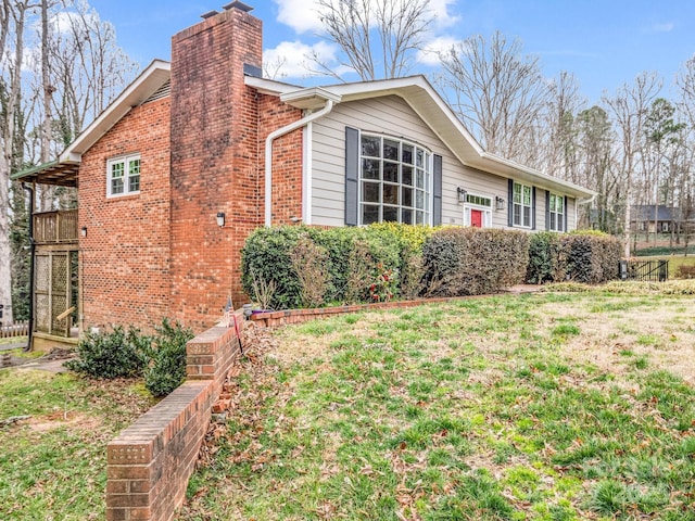 view of side of property with a lawn, a chimney, and brick siding