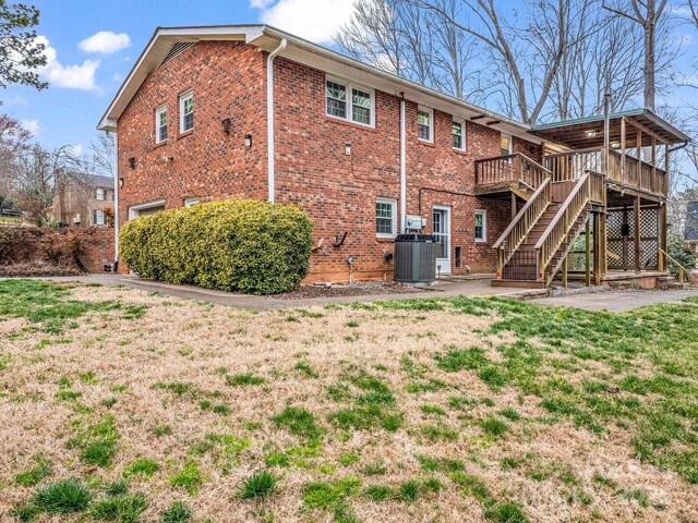 rear view of property featuring stairway, a deck, brick siding, cooling unit, and a yard