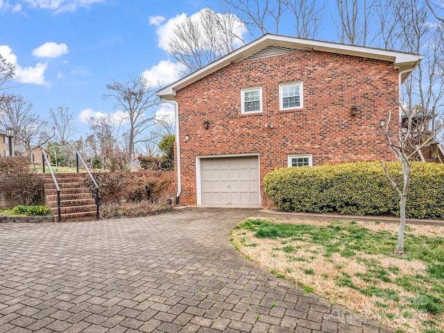view of side of home with decorative driveway, an attached garage, and brick siding