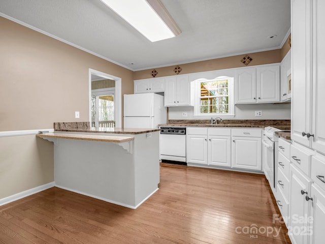 kitchen featuring white appliances, white cabinetry, a kitchen breakfast bar, and a peninsula