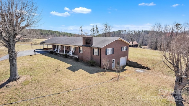 back of property featuring covered porch, driveway, a lawn, and an attached garage