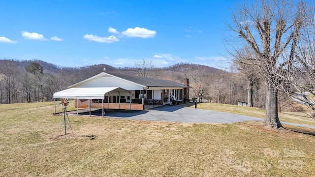 rear view of property featuring driveway, a yard, a carport, and a mountain view