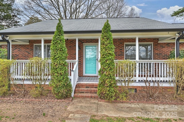 view of front facade with covered porch, roof with shingles, and brick siding